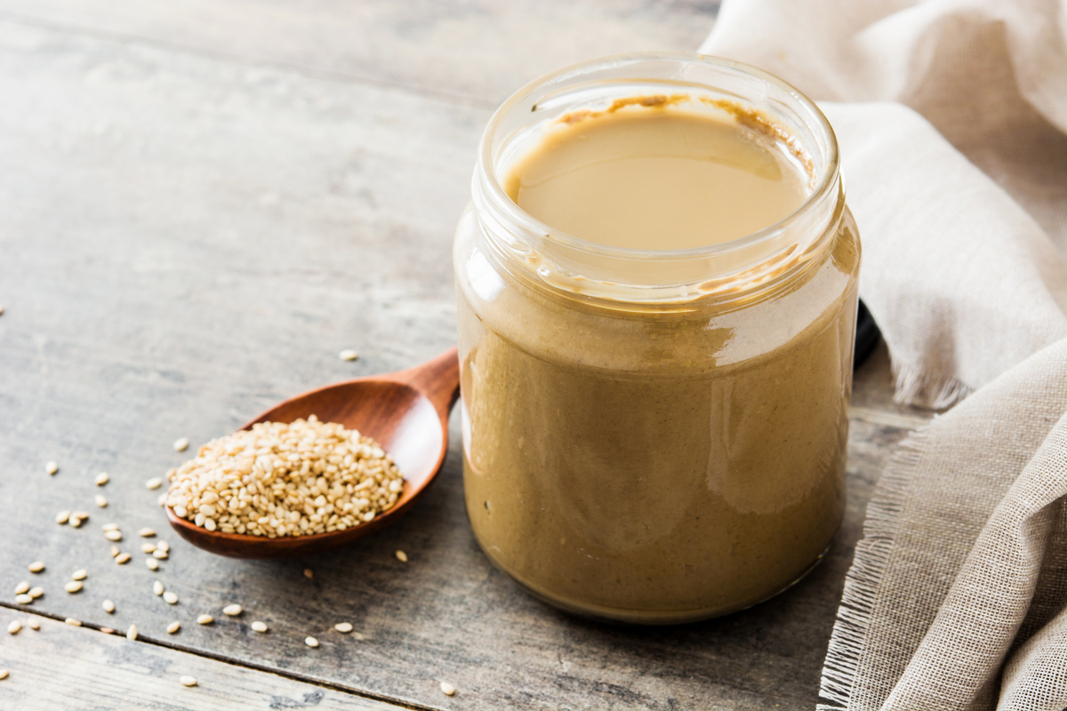 Tahini and sesame seeds on wooden table.