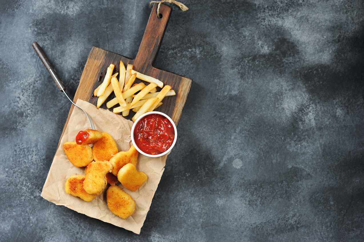 Chicken nagets on a wooden board. Rgdom with nuggets french fries and ketchup sauce. View from above. Free space for text.